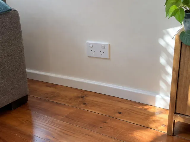 White double power point on a painted wall above timber floorboards in a living room in Kanwal