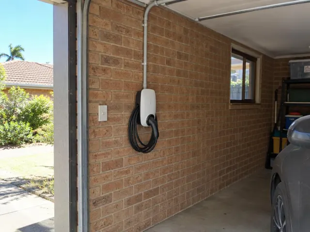 Wall-mounted EV charger with coiled cable on a brick garage wall beside a parked car in Charmhaven