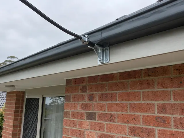 Overhead service cable and bracket on a brick house exterior with gutter and window in Kanwal